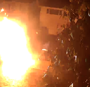 A flame erupting from a vehicle with a man running away while his arm and leg are on fire.