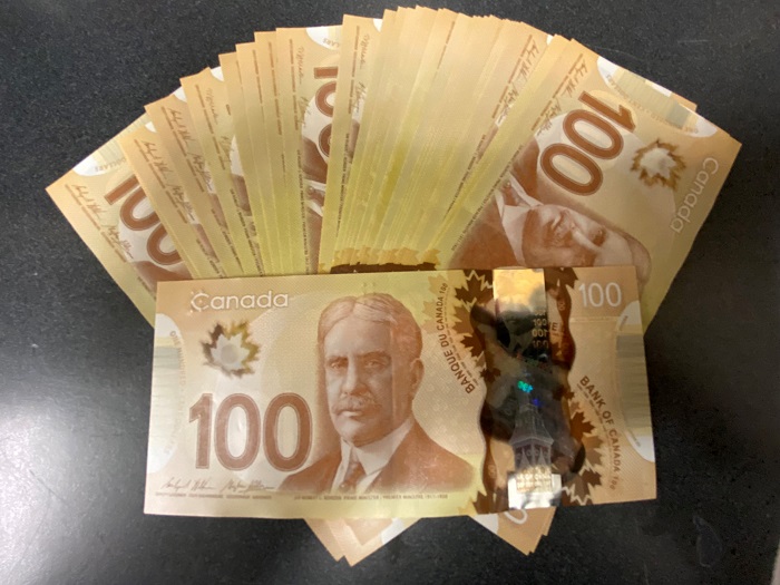 Des billets canadiens de 100 $ trouvés sont disposés en éventail sur une table.