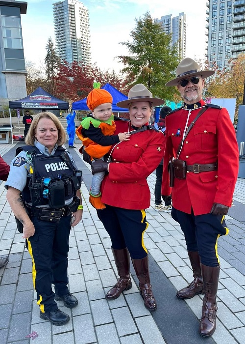 Constable Chantal Mitchel and Constable Glen Tjernagel standing with Constable Sandra Morse holding her son, who is dressed in a pumpkin costume.