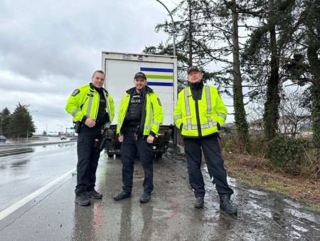 Photo of three enforcement officers standing in front of a commercial vehicle on the side of the road