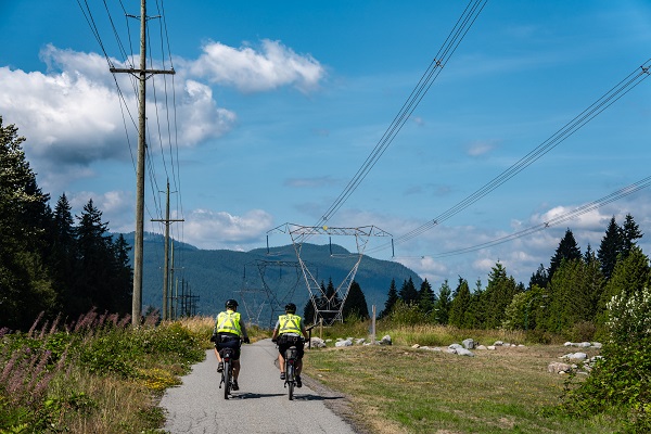 Deux patrouilleurs à vélo sur un sentier, sous des lignes de transport d’électricité.