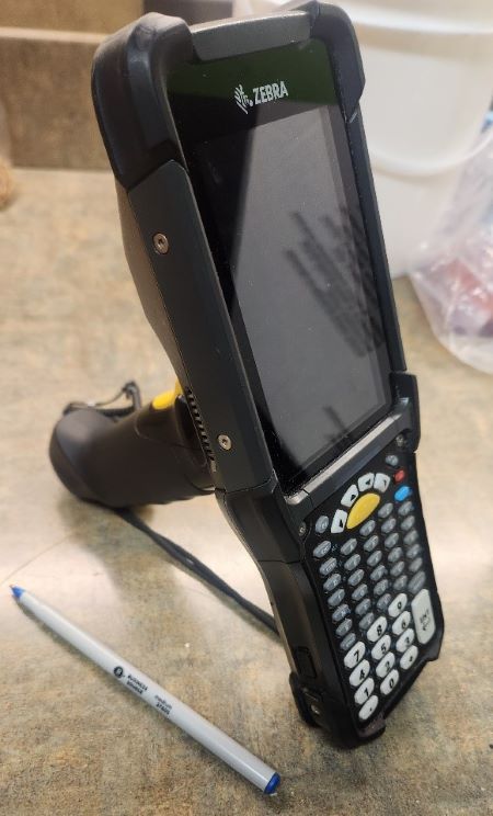 The produce scanner is a: Zebra model, black device with buttons, handle grip mid-way down the back.
