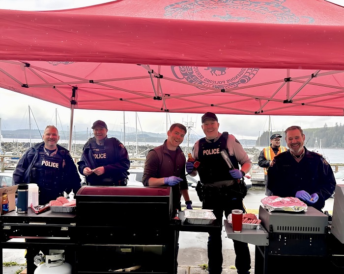 RCMP officers under a tent, cooking BBQ