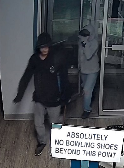 Deux suspects qui entrent par une porte en verre. L’un d’eux porte un chandail noir à capuchon, et l’autre, un chandail gris à capuchon.