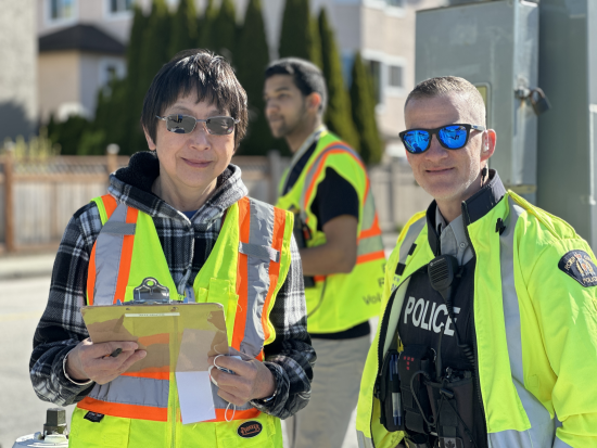 RCMP officer standing with a volunteer wearing a safety vest and holding a clipboard