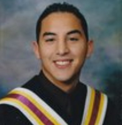 Photo d’un adolescent de 17 ans qui a de courts cheveux noirs et qui porte une toge de finissant noire arborant des bandes blanches, jaunes et rouge foncé. Le jeune homme sourit.