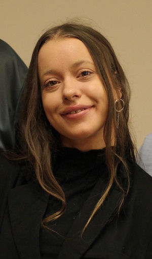 A woman wearing a black turtle neck long-sleeved shirt, hazel eyes and long brown hair