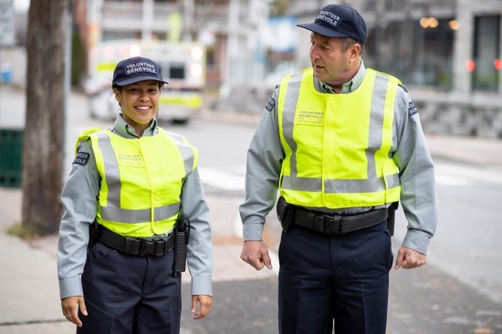 deux bénévoles auxiliaires en uniformes avec gilets réflecteurs sur un trottoir.
