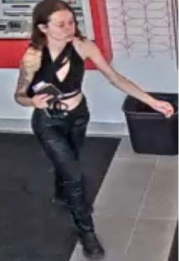 A woman wearing a black cropped tank top and black pants with a tattoo on her right arm walking indoors