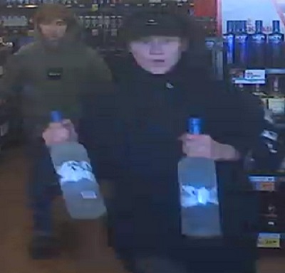 Jeune homme suspect portant un chandail à capuchon noir et une casquette noire transportant deux grandes bouteilles de vodka Grey Goose