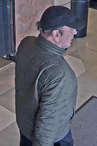 Man wearing a dark-green jacket and black ball cap, suspected of shoplifting.