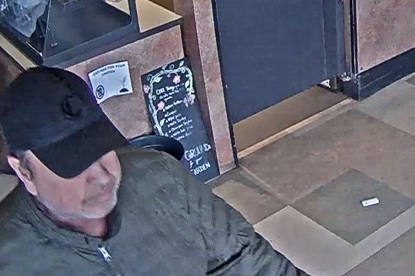 Man wearing a dark-green jacket and black ball cap, suspected of shoplifting.