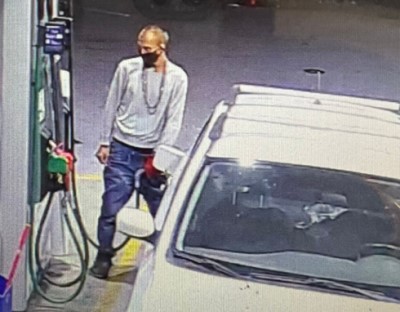 Suspect male wearing a grey long sleeve sweater, jeans, a black mask and long chain necklaces around his neck, pumping gas into a white Subaru