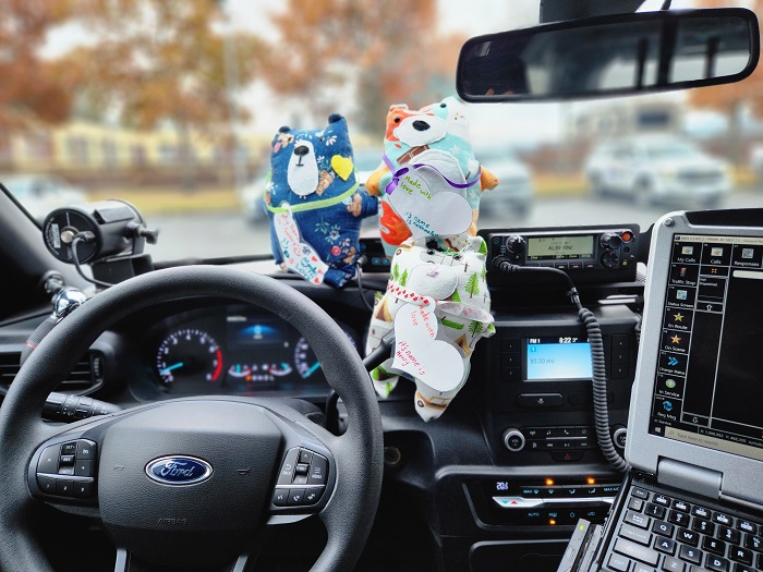 Hand-sewn bears sitting in a police car.