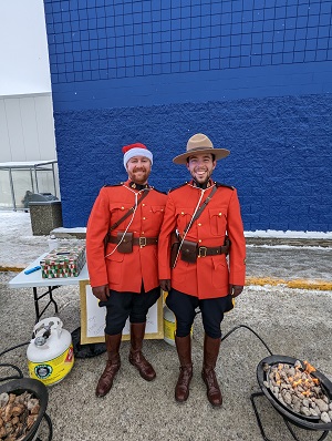 Photo of two RCMP officers in red serge standing by a table. One officer is wearing a Santa Clause hat. 