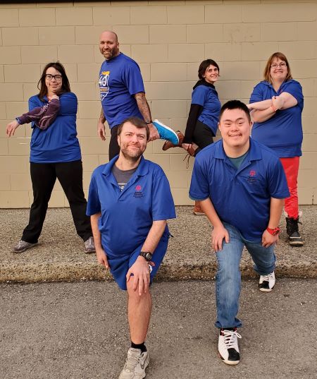 At the back, second from the left, Cst. Phil Whiles is getting ready for the Law Enforcement Torch Run with the support of five Kamloops Special Olympians. In running shoes and blue shirts, the group members complete various arm and leg stretches in preparation.