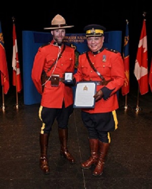 Superintendent Lee wearing red serge presents an award to Constable Stewart also in red serge