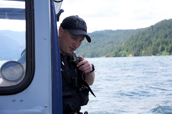 Cst Kyle Toole speaks into his portable police radio while navigating the BC RCMP Zodiac boat on Harrison Lake.
