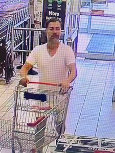 Le troisième suspect pousse un chariot dans le magasin. Il porte un t shirt blanc à encolure en V et un short de couleur pâle. Il a les cheveux foncés courts et porte une barbe grisonnante ou naissante. 