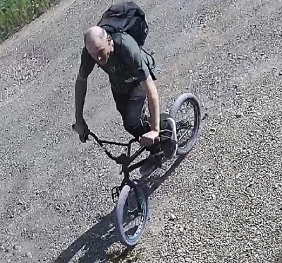 balding man with short hair riding a BMX bike with purple tires wearing a black backpack