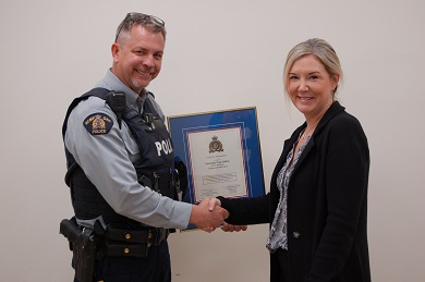 Cst. Troy Collins and Paula Pepin display the framed award as they shake hands