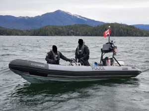 A police boat with two West Coast Marine members on it with mountains in the background