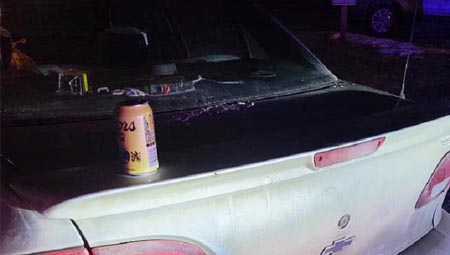 Une photo de nuit de l’arrière d’une voiture avec sur le coffre une canette de bière Coors. 